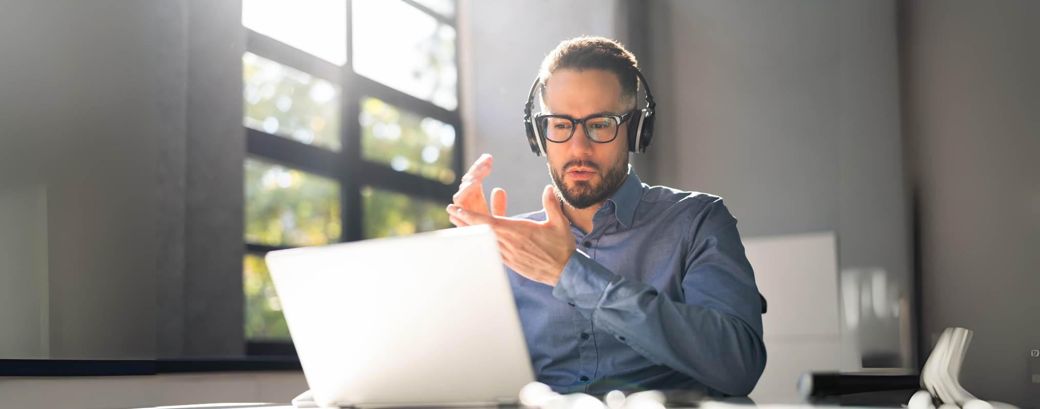 Mann sitzt mit Headset vor Computer und gestikuliert, ist offenbar in einem Onlinemeeting